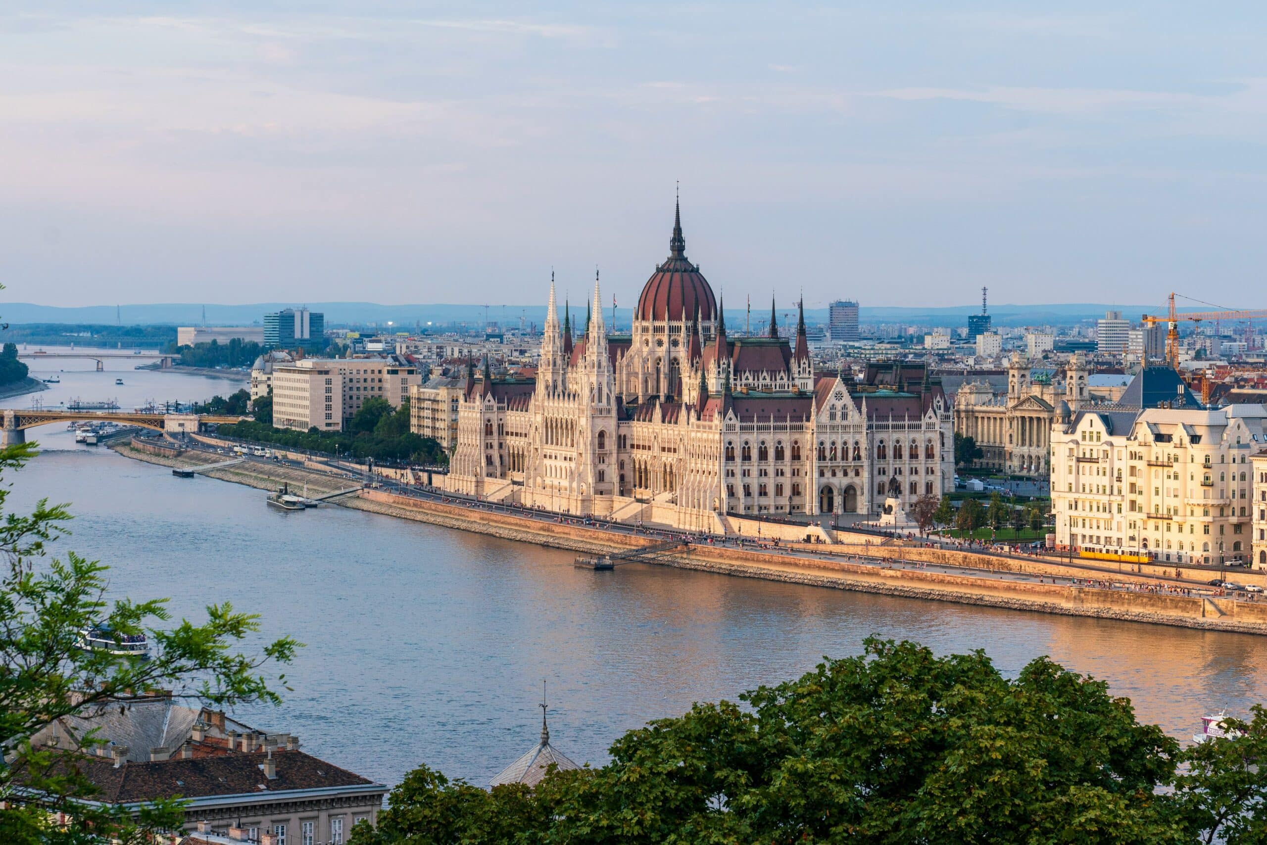 Budapest Parliament Building with a red dome along the Danube River, photographed from a hillside viewpoint.