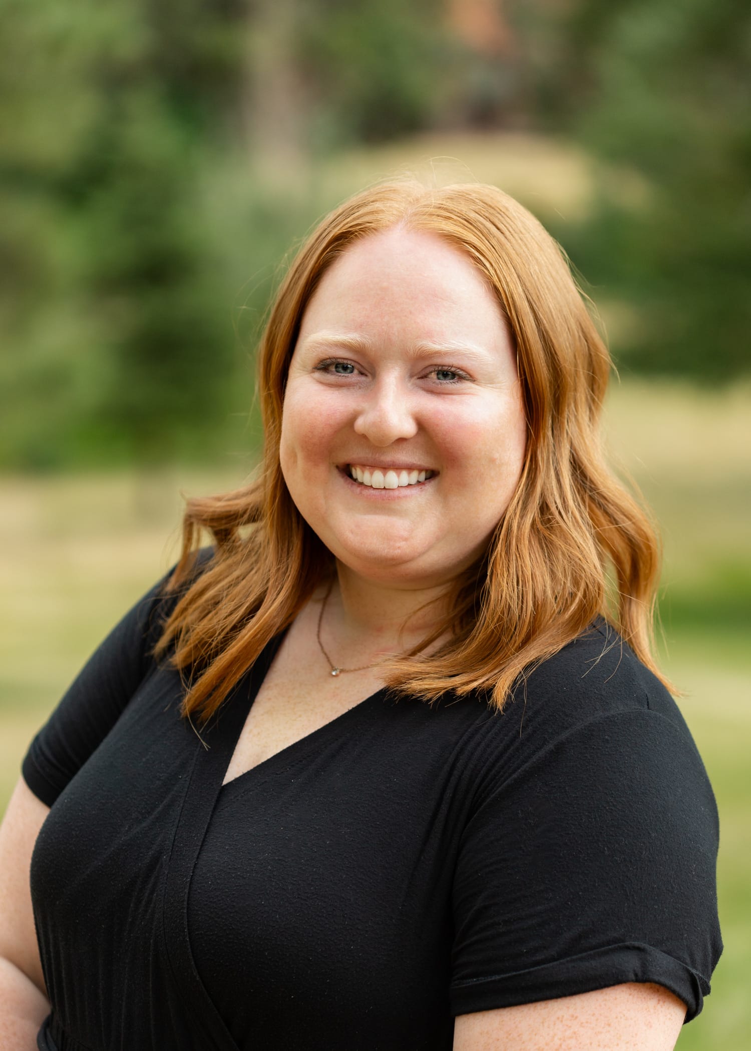 Portrait of a smiling woman with red hair wearing a black top outdoors.