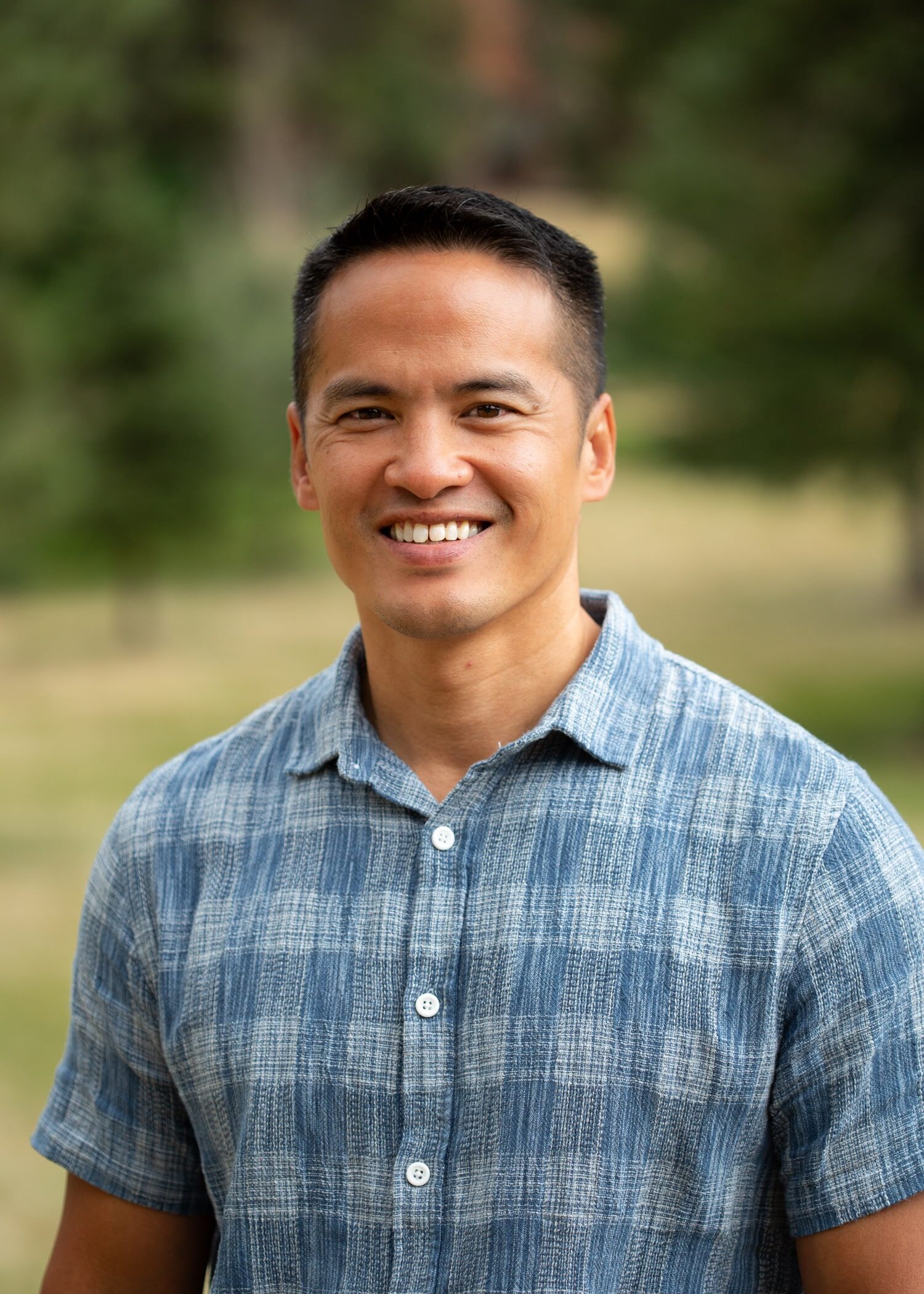 Smiling man with short black hair in a blue striped button-down shirt outdoors.