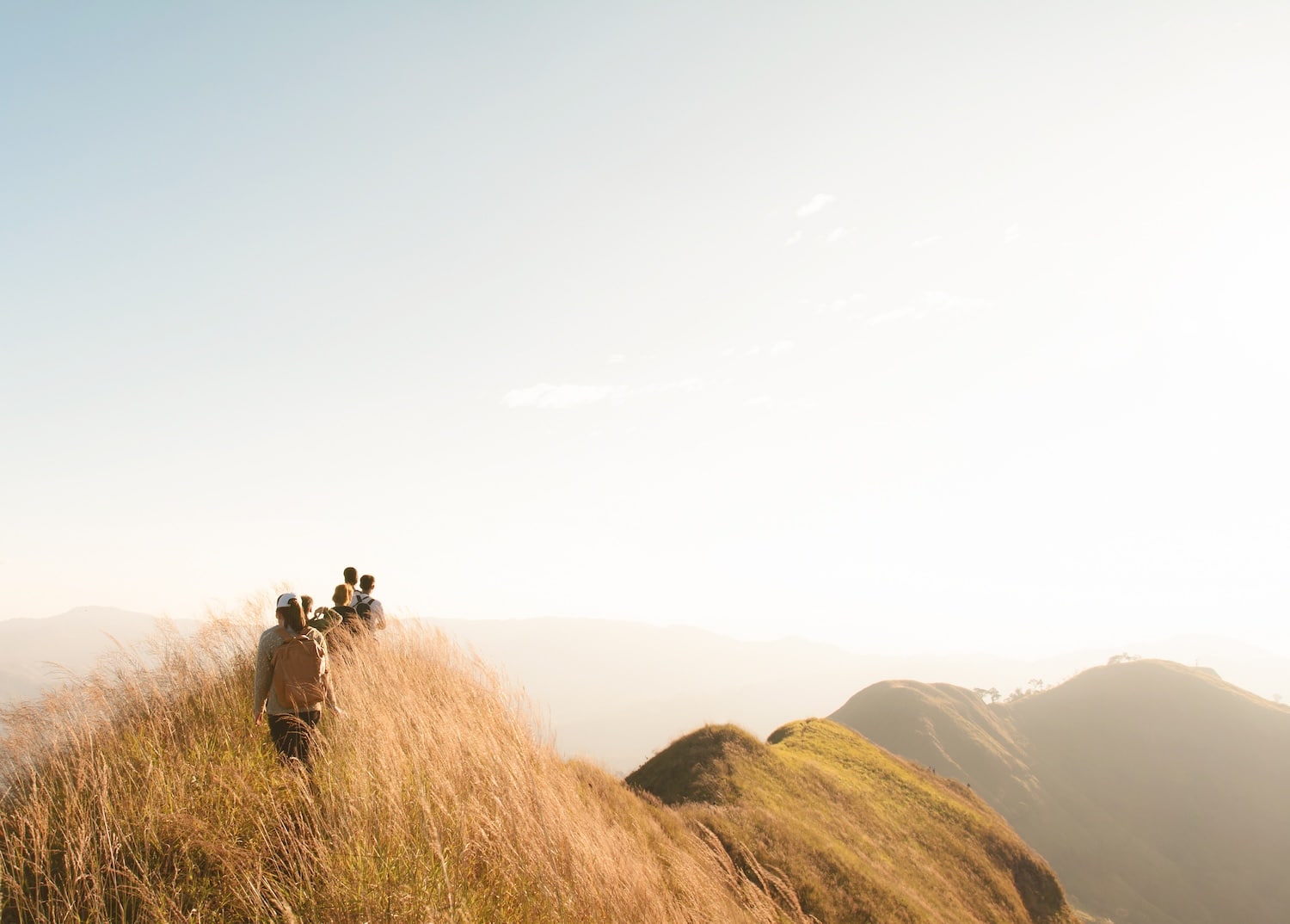 Group of hikers walking along a grassy ridge at sunset on a mountain trail