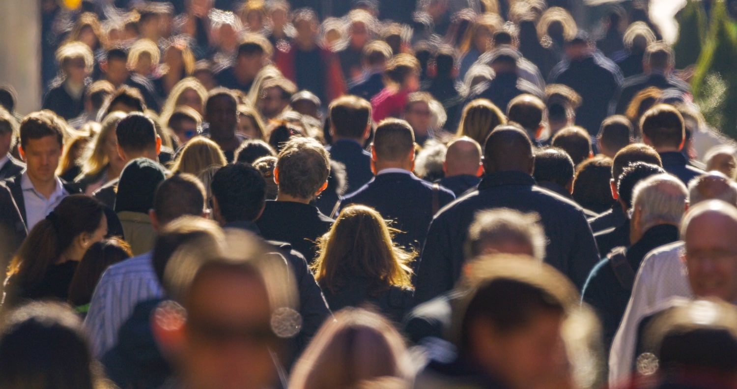 Crowded city street with people walking away, backs facing the camera in daylight to form a dense crowd
