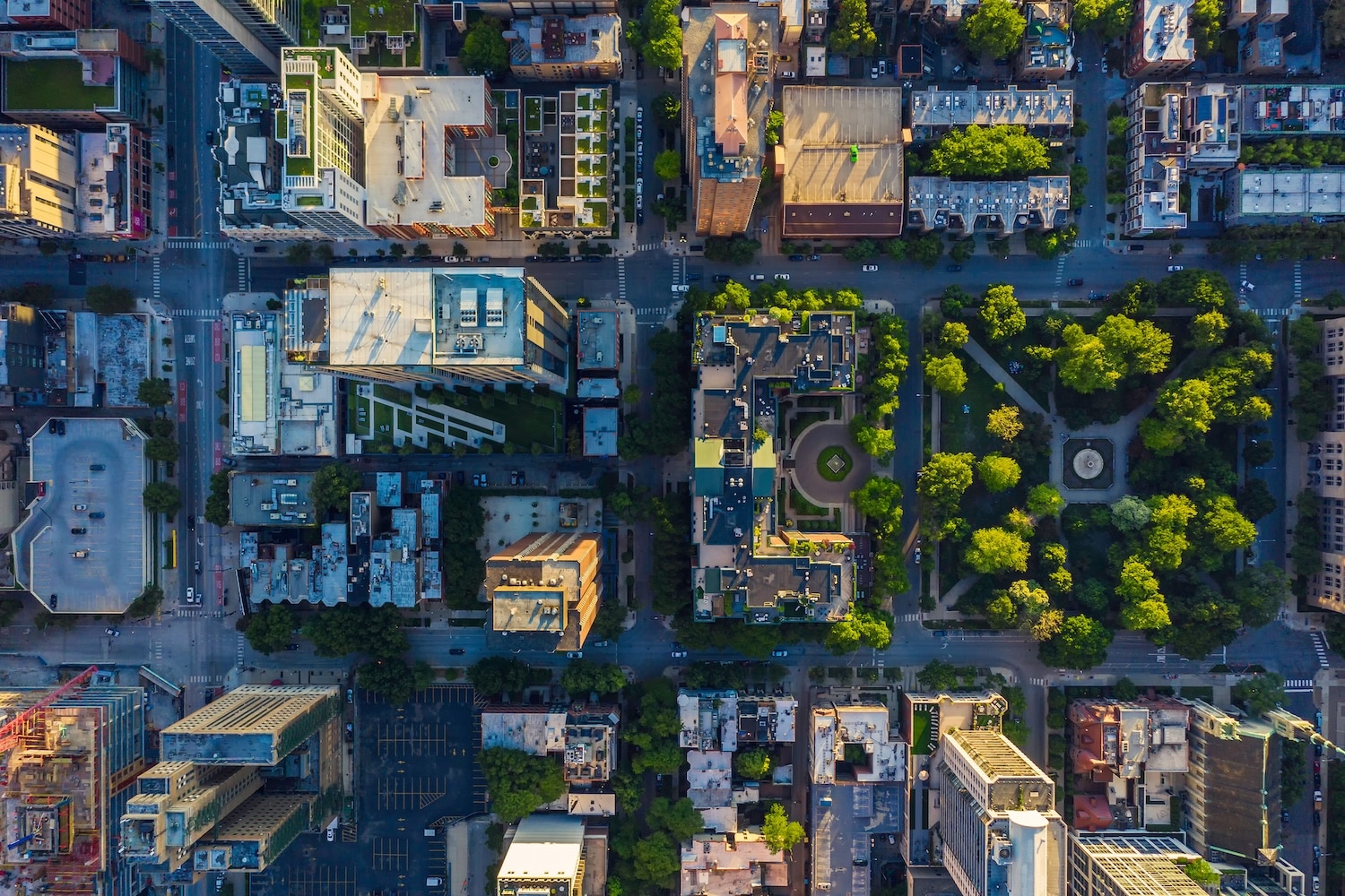 Aerial view of a city grid showing tall buildings, streets, and a large central park with circular paths and dense green trees.