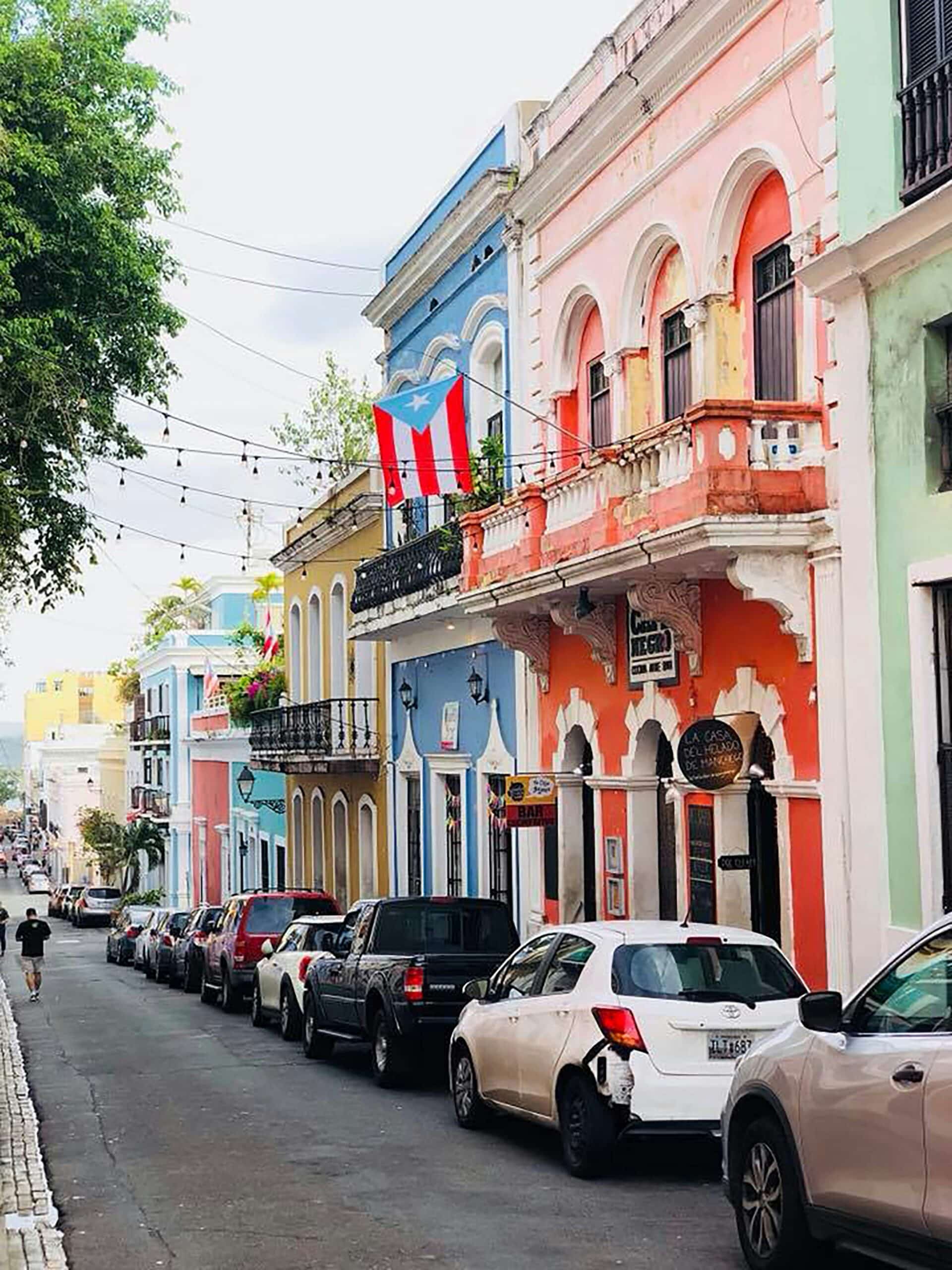Pastel-colored colonial buildings line a narrow street, with string lights and a Puerto Rican flag.