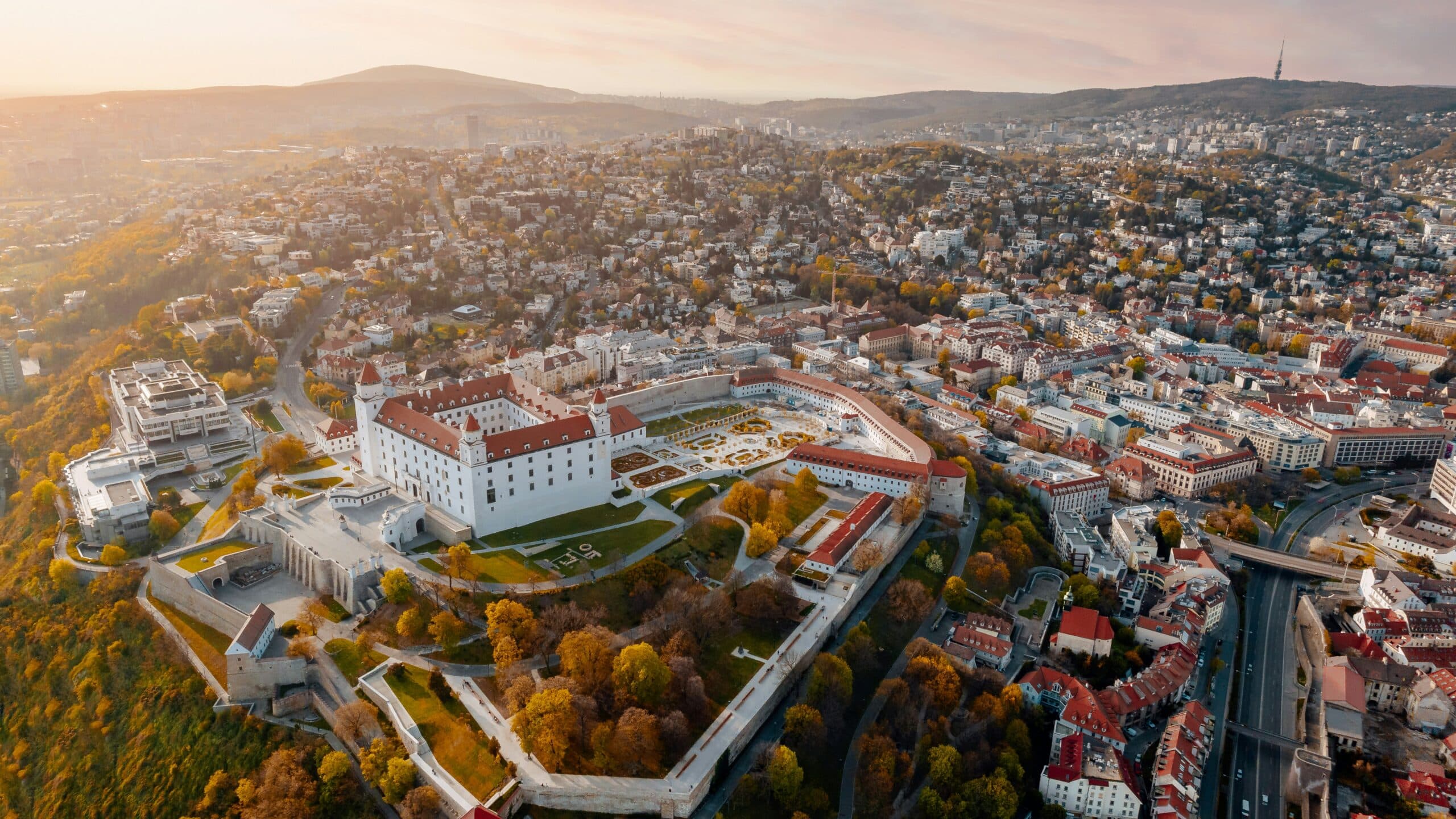 Aerial view of Bratislava Castle on a hill overlooking a autumn-colored city at sunset in golden light